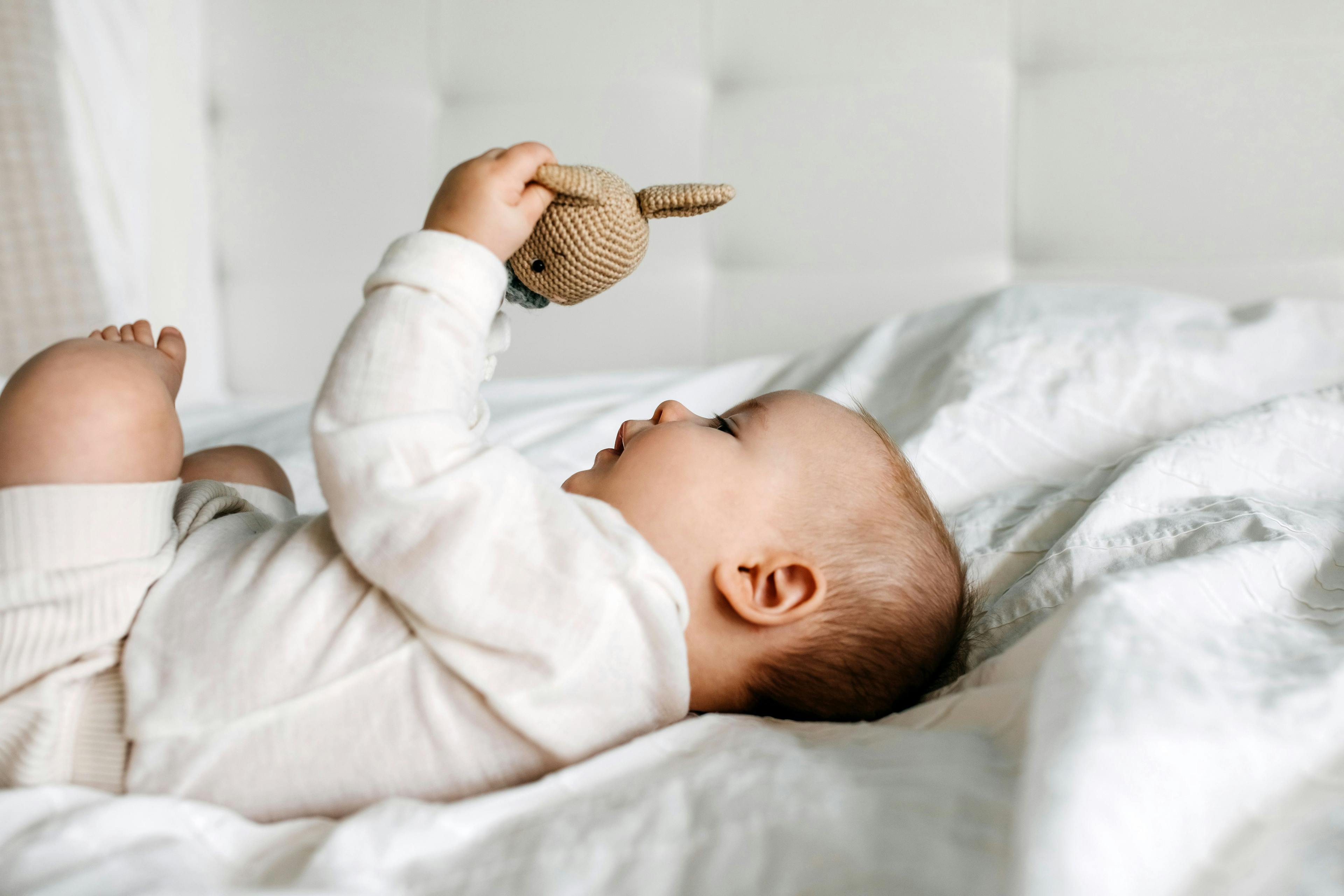 Five months old baby lying on bed, playing with a crocheted bunny toy: © Bostan Natalia - stock.adobe.com