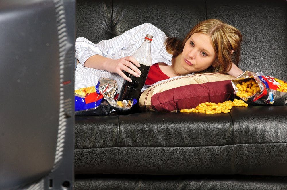 stock image of teen watching TV and eating junk food